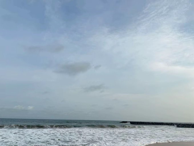 A serene beach scene with gentle waves rolling onto the shore under an overcast sky, evoking the calm "gm" morning vibe the poster references. The tranquil ocean view contrasts with their frustration over "YARD" listing an NFT for over $1,000, capturing the disconnect between peaceful mornings and chaotic crypto markets.