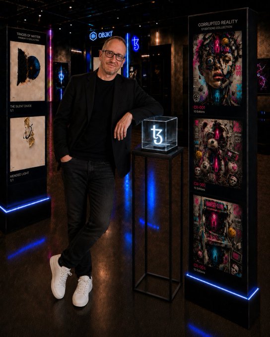 A man poses in a digital art gallery showcasing Tezos NFT collections, including "Corrupted Reality" and "Traces of Matter" displayed on illuminated pillars beside an OBJKT logo display, promoting his objkt.com profile @tz2CMKuT for #TezosTuesday.