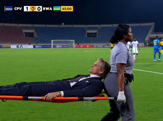 A photo of a man in a pinstripe suit being carried on a stretcher by a medical worker across a soccer field during a match between CPV and RWA, which is tied 1-0 at the 45:00 mark.