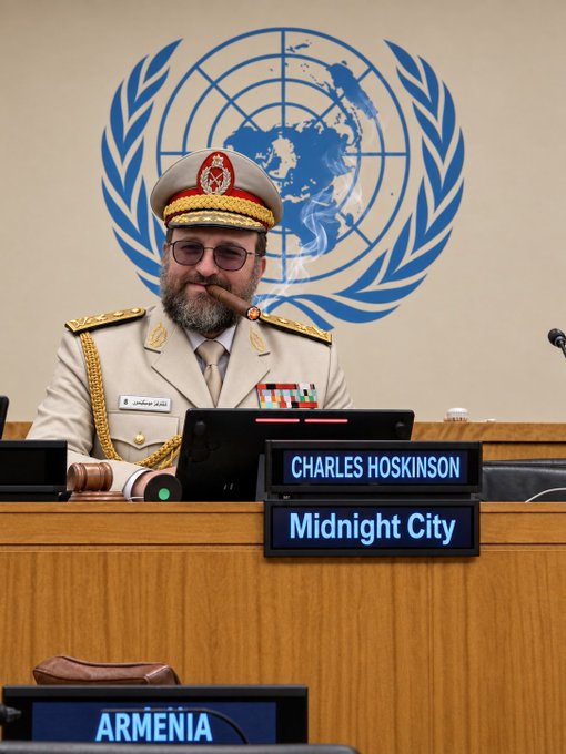 Charles Hoskinson, founder of Midnight City, sits at a UN podium in a ceremonial military uniform with medals, smoking a cigar with a nameplate identifying him and "Midnight City" displayed in front of him, with the "ARMENIA" placard visible in the foreground—visually fitting the caption "Speech at the UN went over well."