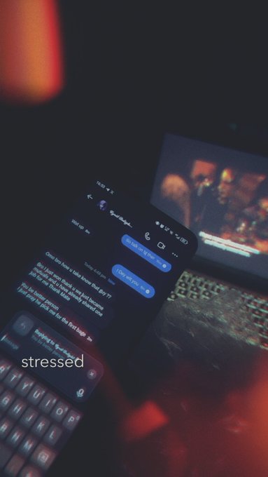 A moody photograph of a smartphone displaying a text conversation about feeling overwhelmed, placed next to a laptop and keyboard in dim lighting with the word 'stressed' overlaid.