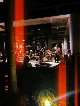 A grainy photograph of a string ensemble performing in a dimly lit, columned interior space, with a red timestamp reading '92.11.18'.