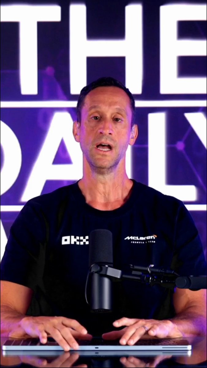 The image shows a man sitting at a desk with a microphone, likely recording a podcast or live stream. He appears to be wearing a black shirt and has his hands on a microphone stand. The background features purple text that reads "THE DAILY" and "MELISSA". There is also a reference to the price of Bitcoin in the image, which suggests that the man might be discussing cryptocurrency-related topics or events.