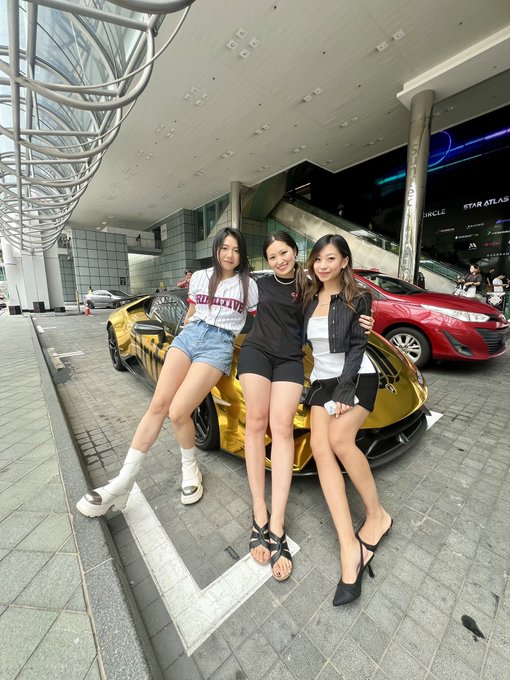 Three young women pose in front of a gold Lamborghini at what appears to be a luxury car display outside the Star Atlas venue, with a red sports car visible in the background. The scene suggests a glamorous automotive or crypto-related event, possibly tied to a sponsorship or promotional appearance for Drift Protocol.