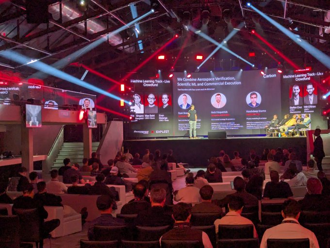 A technology conference panel titled 'We Combine Aerospace Verification, Scientific AI, and Commercial Execution' with speakers discussing 'Machine Learning Track - Live Crowdfunder' on stage before an audience.