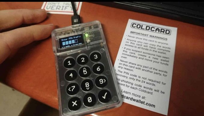 A COLDCARD hardware Bitcoin wallet device displaying 'Enter PIN Prefix' on its small screen, with an important warnings card beside it cautioning that the card can never show seed words and explaining proper security practices.