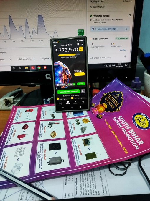 A smartphone displays a Watch2Earn app showing '3,773,970 TOSHI' and 'STAGE 41', resting on a 'Festival Bhavan South Bihar Season Promotion' pamphlet next to a computer monitor.