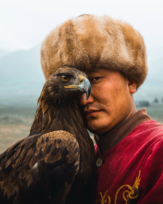 A Mongolian eagle hunter in a traditional fur hat and red velvet robe poses closely with his golden eagle, embodying strength and partnership. The image's themes of focus, tradition, and victory align with the post's encouraging message of having a great weekend and "always win."
