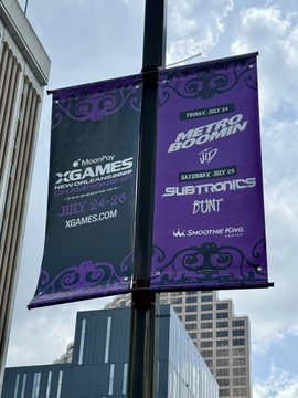 Two purple banners on a lamppost advertise MoonPay's XGAMES New Orleans Championship from July 24-26 at XGAMES.COM, alongside a "Melvin Boo" event with Subtronics and PONT on Friday, July 25 and Saturday, July 26 at Smoothie King Center. This aligns with the "MoonPay NOLA" post, highlighting MoonPay's branded signage promoting their events in New Orleans.