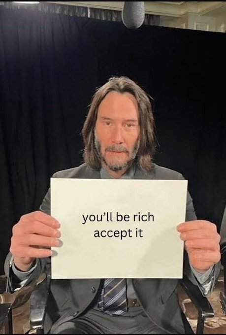 Keanu Reeves holds a white sign with the text "you'll be rich accept it" printed on it.