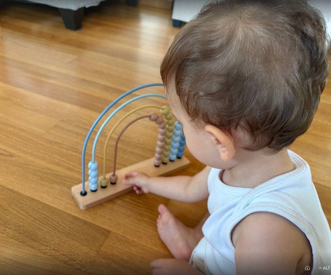 A baby playing with a wooden abacus toy with colorful beads on a wooden floor.