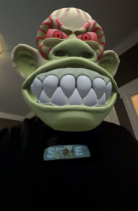 A person wearing a black sweatshirt using a green monster mask filter (resembling a Donkey Kong-like character with red eyes and large teeth) with 'SMIRAE' visible on their shirt.