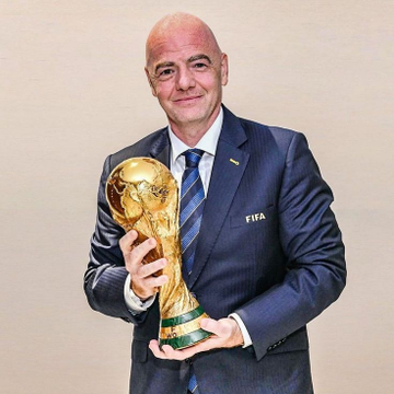 A man in a dark "FIFA" suit proudly holds the golden FIFA World Cup trophy. The image connects to the post by tying the prominent FIFA figure to the high-stakes World Cup bet on Argentina vs. England.