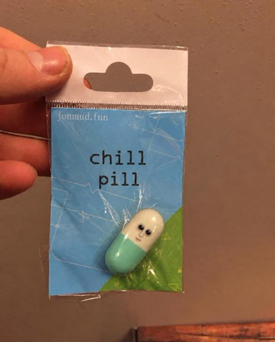A hand holds a small packaged figurine labeled 'chill pill' from 'jonmud.fun', featuring a cute pill character with a face.