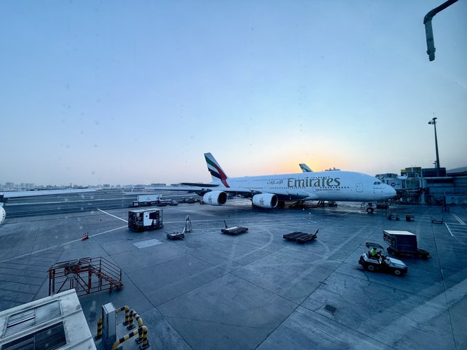 An Emirates Airbus A380 is parked at an airport gate during dawn, with ground equipment and baggage carts scattered around the tarmac, fitting the "gm" (good morning) post as it captures an early morning scene at the airport.