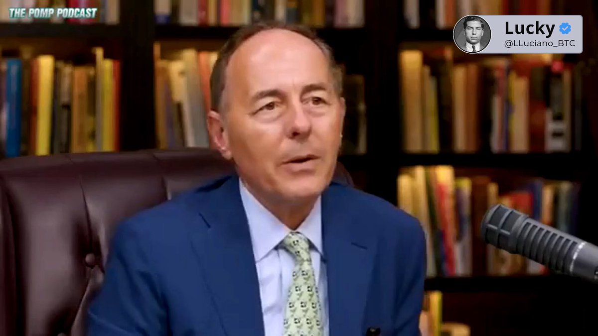 The image features an older man wearing a suit, sitting behind a microphone with his head tilted back as if he's speaking or listening intently. The background shows a bookshelf filled with numerous books arranged in various sizes and colors. The caption on the image reads "Why Bitcoin' s 4-year halving cycle points to 2026 being a year of decline." This statement is related to the man, who could be an expert or commentator discussing the implications of Bitcoin's 4-year halving cycle on its value.
