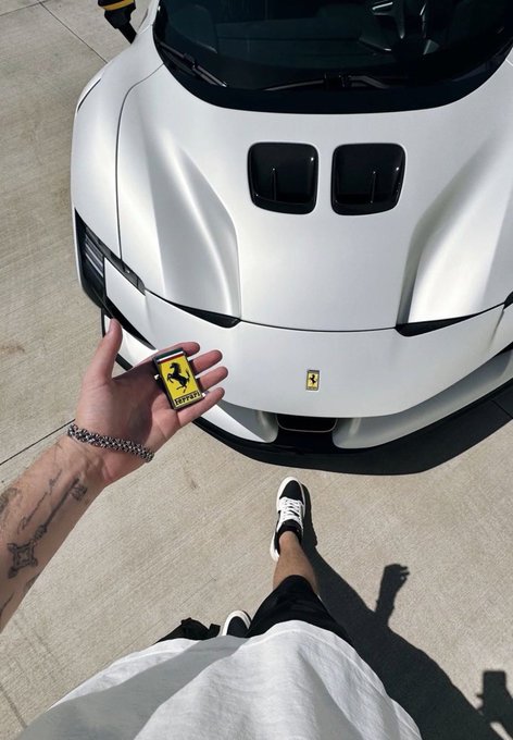 A person holds up a yellow Ferrari key fob in front of a white Ferrari sports car.