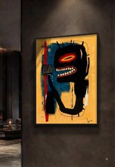 A framed abstract painting with a red, black, and white face-like design hanging on a dark wall next to a shelf with decorative items.
