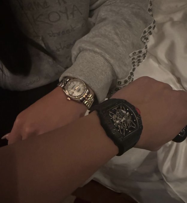 Two people rest their arms side by side, one wearing a silver and gold two-tone watch with a light face, the other sporting a black tonneau-shaped skeleton watch. The image connects to the "Gm friends" greeting by showcasing a casual, friendly wristwatch display perfect for a morning check-in with close friends.