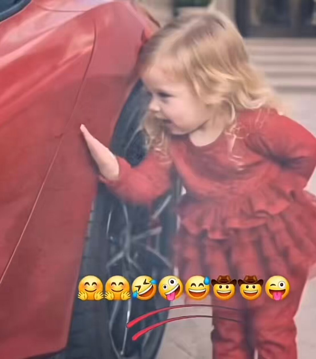 The image features a young girl dressed in red standing next to a car with her hand on its tire. The caption of the image includes a line about the World Cup that seems unrelated to the scene at first glance, but upon closer inspection, it is actually referring to the same event as the girl's outfit. This adds an interesting twist and connection between the girl and the World Cup.