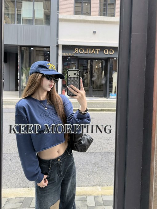 A mirror selfie of a woman wearing a navy blue cropped sweater with 'KEEP MORPHING' text, a navy cap, sunglasses, and a denim skirt, posing in front of a 'GD TAILOR' shop.
