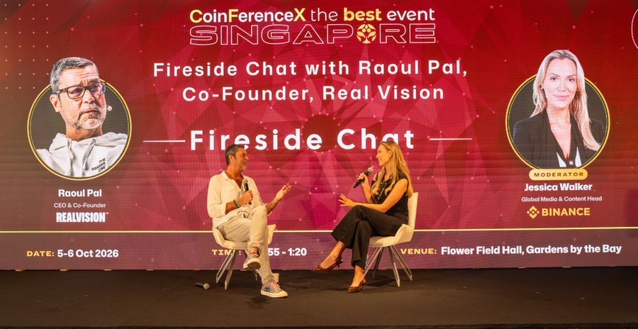 A man and woman sit on white chairs on stage at CoinFerenceX Singapore, in front of a backdrop featuring their headshots and text: "Fireside Chat with Raoul Pal, Co-Founder, Real Vision" and "Moderator: Jessica Walker, Global Media & Content Head, Binance," with event details noting 5-6 Oct 2026 at Flower Field Hall, Gardens by the Bay.