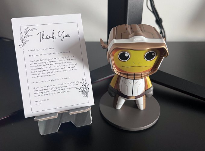 A small wooden toy figure of a character in a hooded outfit displayed next to a 'Thank You' note from the creators.