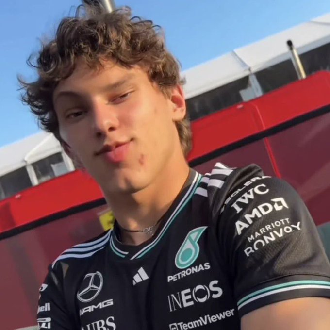 A young man wearing a Mercedes-AMG Petronas F1 team shirt (featuring IWC, AMD, Marriott Bonvoy, INEOS, and TeamViewer logos) sticks his tongue out at the camera.