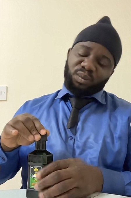 A man in a blue dress shirt, black tie, and black beanie sits at a table with his eyes closed, holding a pump bottle of hand sanitizer.