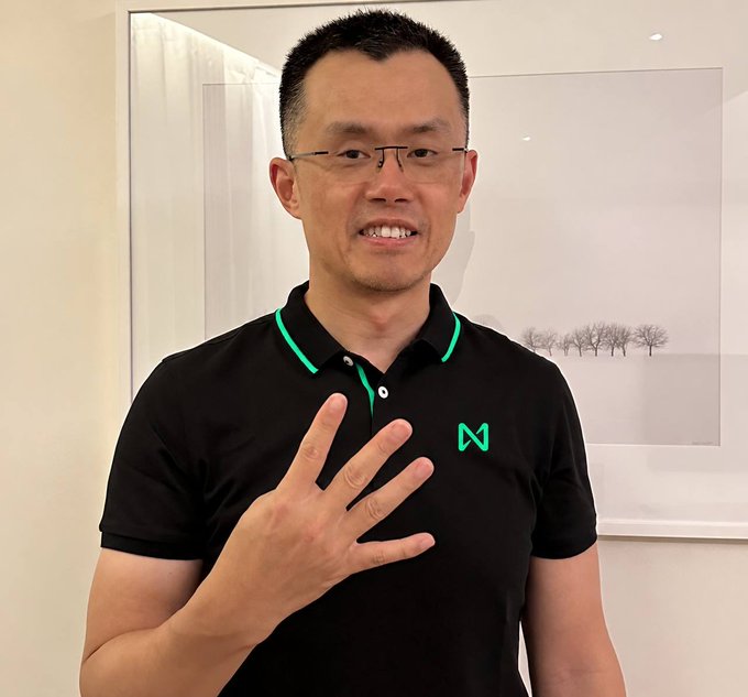 A man wearing glasses and a black polo shirt with green trim and a green "N" logo on the chest holds up his hand, gesturing while speaking.