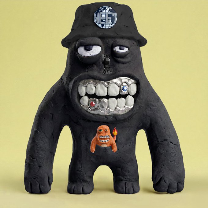 A black, claymation-style monster figure wearing a "NEET" cap with an ON/OFF switch between its droopy eyes and a wide grin featuring silver-capped teeth, while a smaller orange creature holding a torch is embedded in its chest. The quirky, handcrafted "internet magic jpeg" aesthetic of the sculpture mirrors the playful, collectible NFT art vibe referenced in the post.