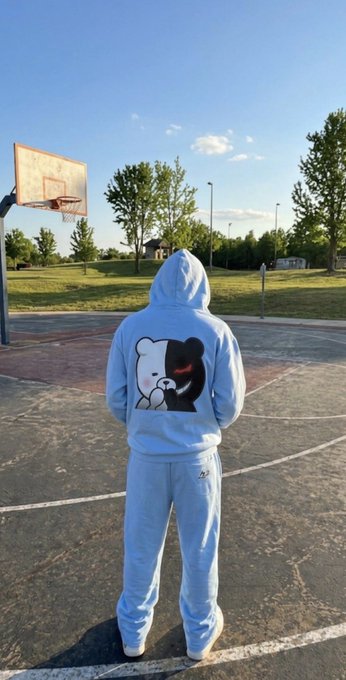 A person standing on an outdoor basketball court wearing a light blue tracksuit with a black and white bear graphic on the back of the hoodie.