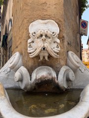 A stone fountain featuring a carved lion's head spout pouring water into a basin below.
