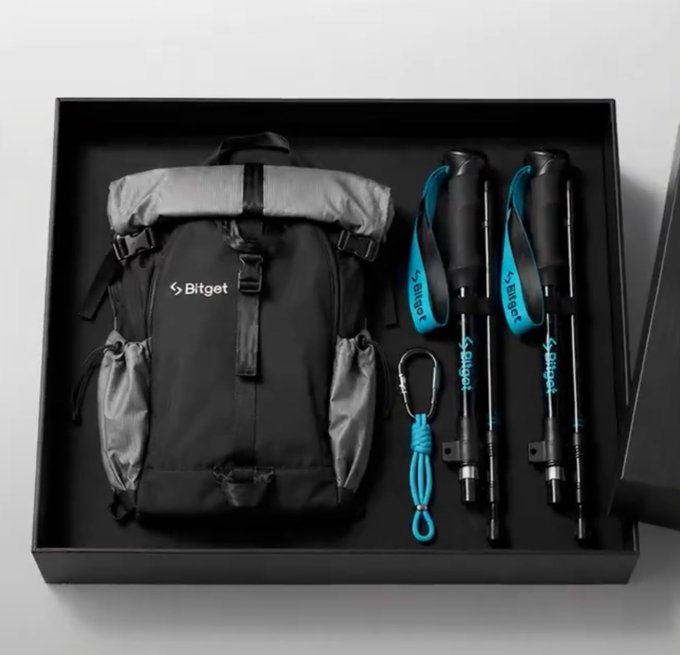 A black gift box containing a "Bitget" branded backpack, two trekking poles, and a blue carabiner rope.