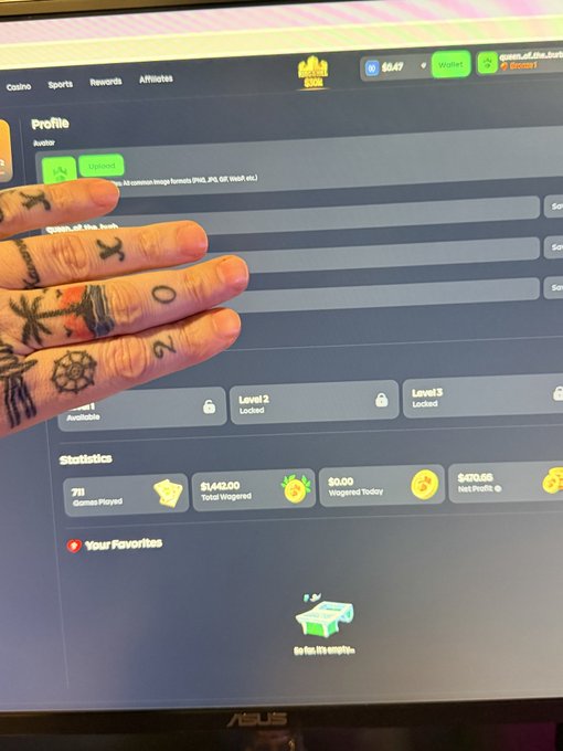 A tattooed hand held up in front of an ASUS computer screen displaying a profile page with statistics showing 71 Games Played, $1,149.00 Total Wagered, and $0.00 Wagered Today.