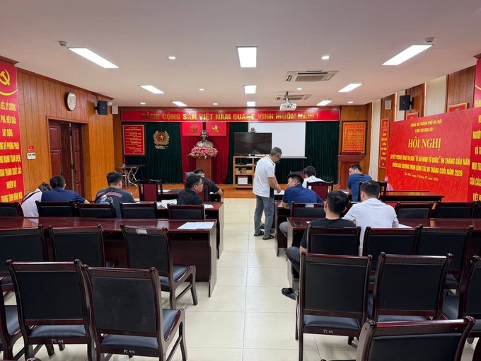 A meeting room with people seated in black chairs facing a stage with a red banner reading 'ĐẢNG CỘNG SẢN VIỆT NAM QUANG VINH MUÔN NĂM' and another red banner on the right labeled 'HỘI NGHỊ' for a conference on 'Ứng dụng AI trong lĩnh vực an ninh quốc gia.'