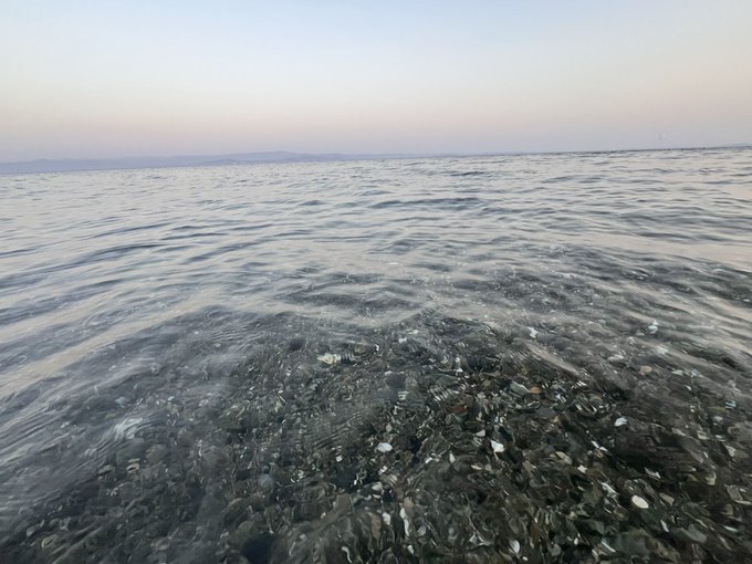 View of clear ocean water with a pebbly shoreline visible beneath the surface at dusk or dawn.