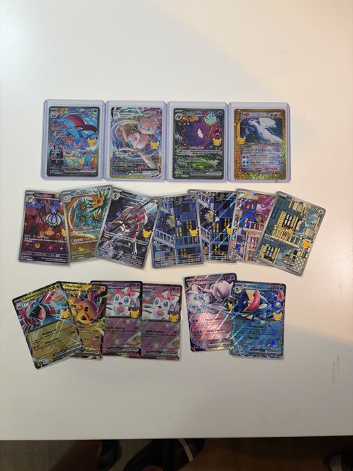 A collection of Pokémon trading cards, including holographic Gyarados, Lugia, Mewtwo, and various stadium/trainer cards, are spread across a white table to celebrate the opening of three additional Elite Trainer Boxes (ETBs).