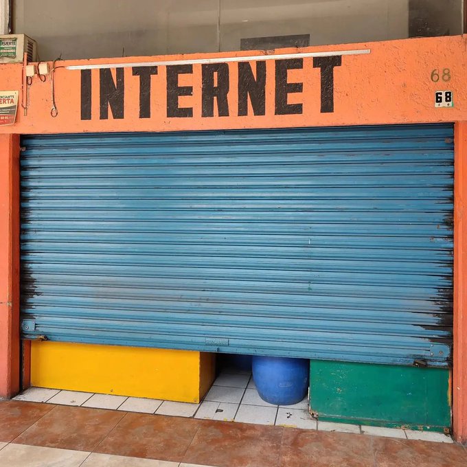 A closed storefront with an orange sign reading 'INTERNET' above a blue metal roll-down shutter, with a yellow, blue, and green painted base.