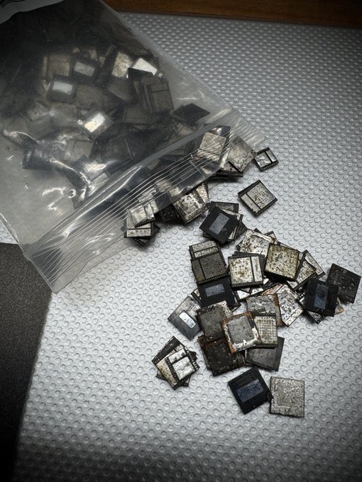 A clear plastic zip-top bag lies open on a white textured surface, with numerous discarded square computer processor chips spilling out onto the surface.