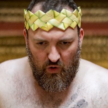 A bearded man with a focused, intense expression wears a handcrafted crown made from folded green leaves or plant material, while the accompanying post discusses Cardano Foundation's technical advancement with BLS12-381 cryptography—a visual metaphor possibly suggesting "kingdom" or "royalty" of blockchain technology, fitting the tone of a significant enterprise-grade upgrade announcement.