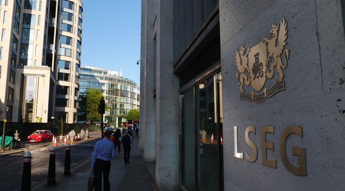 The exterior of a building displays the 'LSEG' (London Stock Exchange Group) logo with a coat of arms featuring griffins on the stone facade, with pedestrians walking on the sidewalk and city buildings in the background.