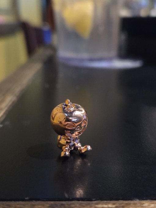 A small chrome/metallic figurine of a character with a crown sitting on a black surface.