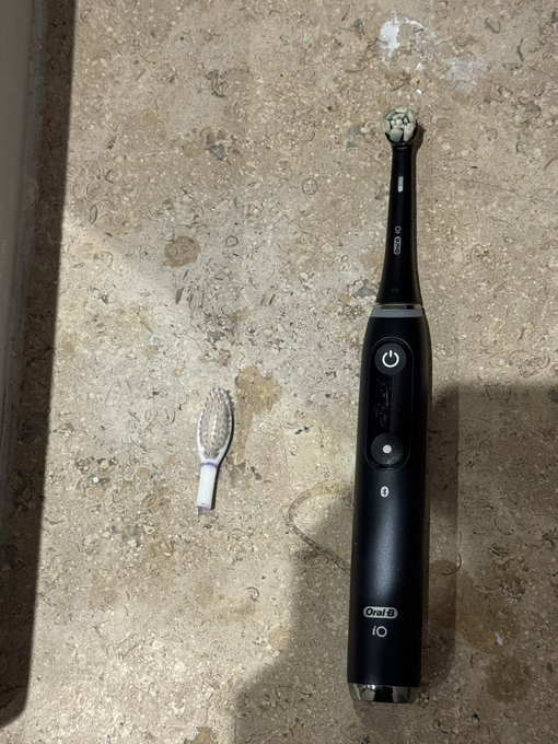 An Oral-B iO electric toothbrush sits next to a worn-out manual brush head on a countertop, illustrating the post's humor about the upgrade you can't trade against.
