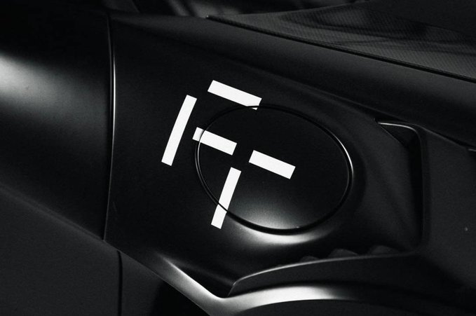 A close-up black-and-white image of a car's fuel cap featuring a white geometric logo, representing the Frontier brand (@JoinFrontier) referenced in the accompanying post. The sleek automotive design suggests Frontier's connection to vehicle technology or transportation innovation.