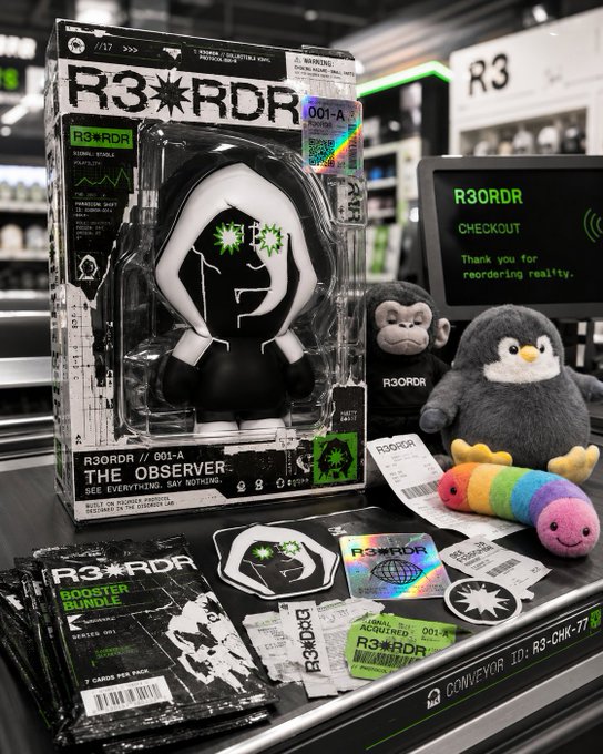 urn of a black and white robot toy, a gray penguin plushie, and a rainbow-colored paper butterfly are displayed on a black shelf with a green "R3rd" sign.
2. A computer monitor is visible to the right side of the frame.