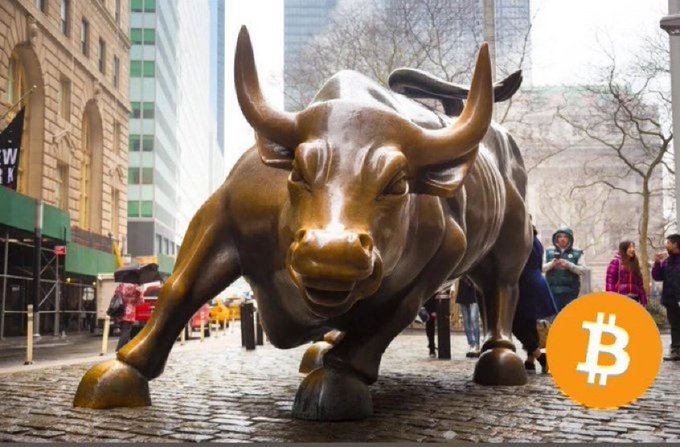 urn of gold bull statue, with horns and mouth open, stands on a cobblestone street, accompanied by people walking past.