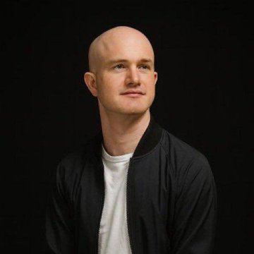 A portrait of a bald man wearing a black bomber jacket over a white t-shirt against a dark background.