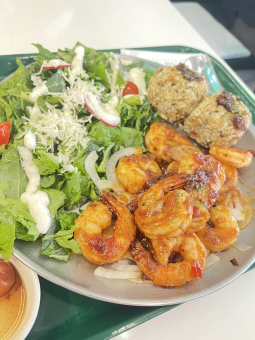 A plate of food featuring cooked shrimp in sauce, a green salad with shredded cheese and dressing, and what appears to be stuffed mushrooms or grain balls.