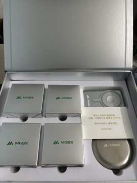 An open MGBX-branded promotional box containing several silver metallic product packages and a circular container.